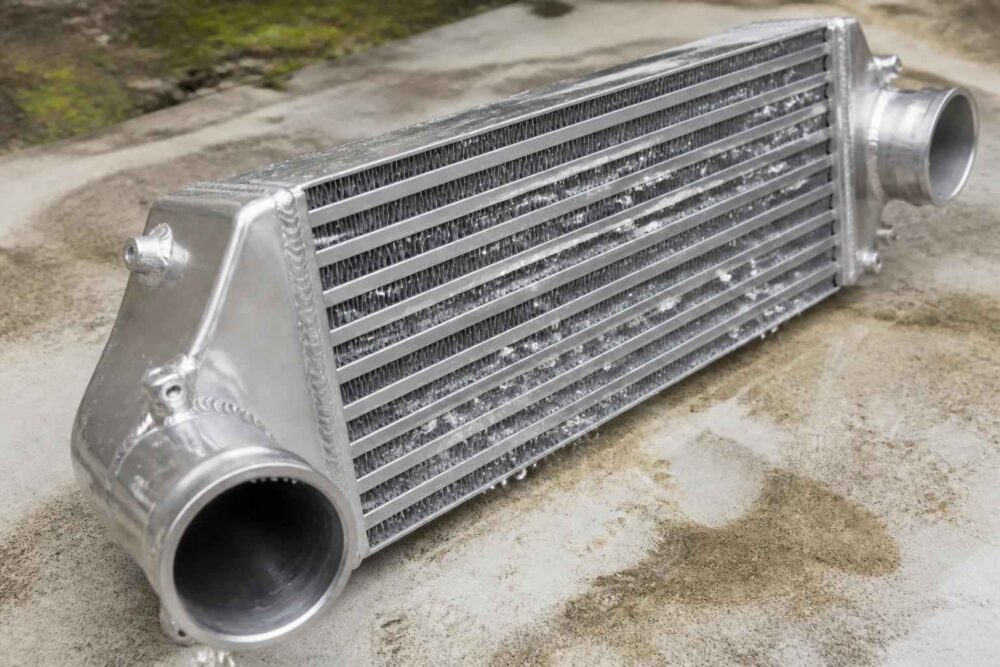Srebrny aluminiowy intercooler z króćcami rurowymi na betonowej nawierzchni