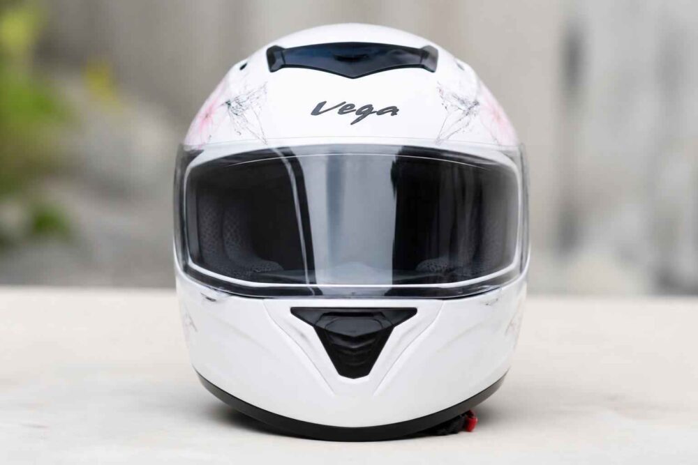 Biały kask integralny Vega z ciemną szybą ustawiony na jasnej powierzchni