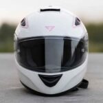 Biały kask motocyklowy z przyciemnianą szybą ustawiony na szarej nawierzchni