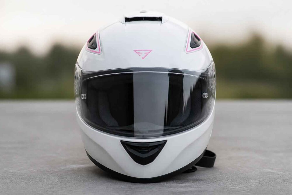 Biały kask motocyklowy z przyciemnianą szybą ustawiony na szarej nawierzchni