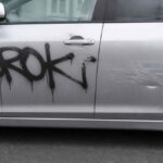 Czarne graffiti i zarysowania na drzwiach srebrnego samochodu-cmpr