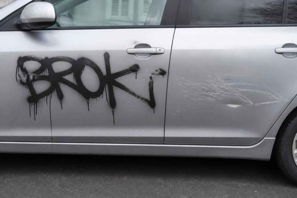 Czarne graffiti i zarysowania na drzwiach srebrnego samochodu-cmpr