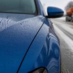 Krople deszczu na niebieskim samochodzie, w tle ciężarówka na mokrej drodze