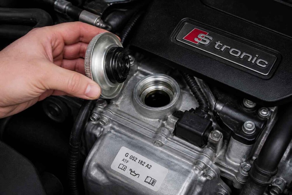 Dłoń trzyma metalowy korek nad otwartym wlewem oleju silnika Audi S tronic
