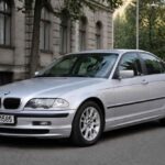 Srebrne BMW serii 3 zaparkowane przy zabytkowym budynku i alei drzew